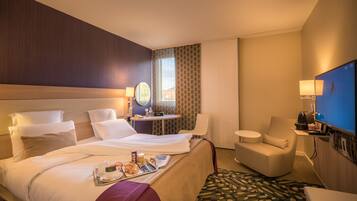 A hotel room with a large bed, a small desk, a chair, and a TV.