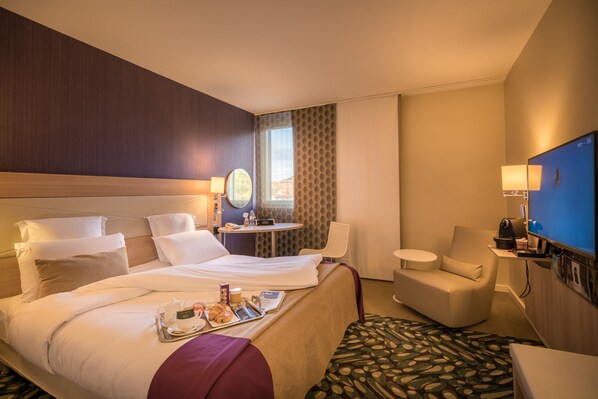 A hotel room with a large bed, a small desk, a chair, and a TV.