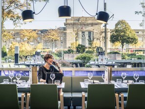 A restaurant with tables set for dining, a waiter, and a view of a building with a sign.