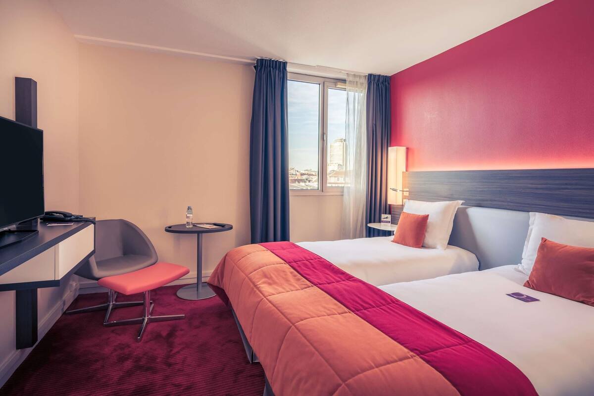 Habitación de hotel con cama, escritorio, silla, una mesita con una botella de agua y una lámpara.