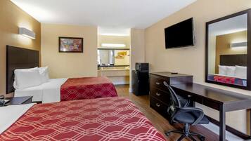 Habitación de hotel con dos camas, un escritorio, una silla, un televisor, un espejo y una kitchenette al fondo.
