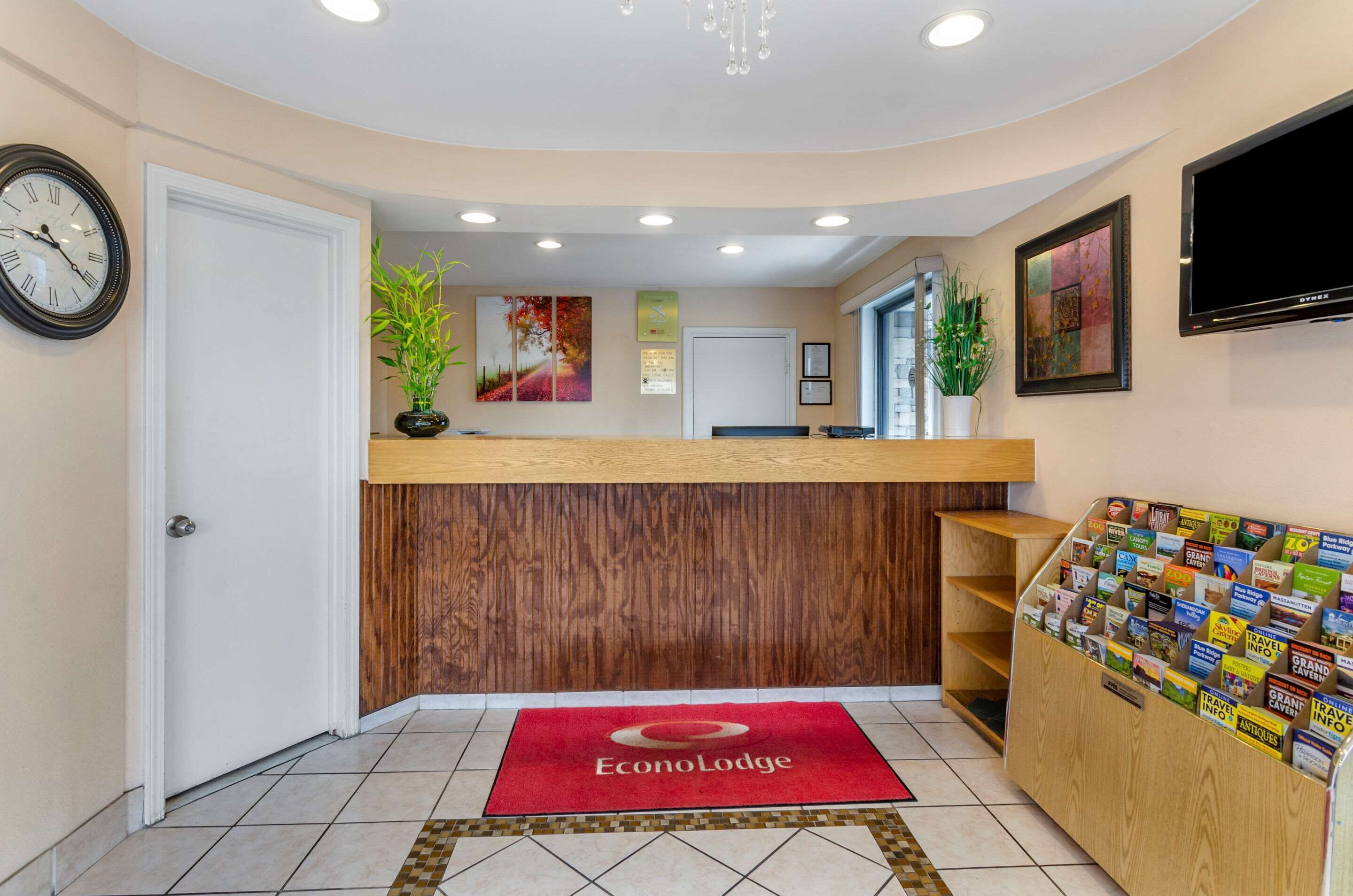 A reception area with a wooden counter, a red carpet with the logo, a clock, and a wall-mounted TV.