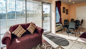 A living room with a sofa, patterned cushions, a dining area with chairs, a table, and a large window with blinds. - Econo Lodge Roanoke Civic Center (Roanoke)