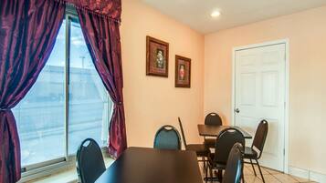 A dining area with a table and chairs, a window with curtains, and two framed pictures on the wall.
