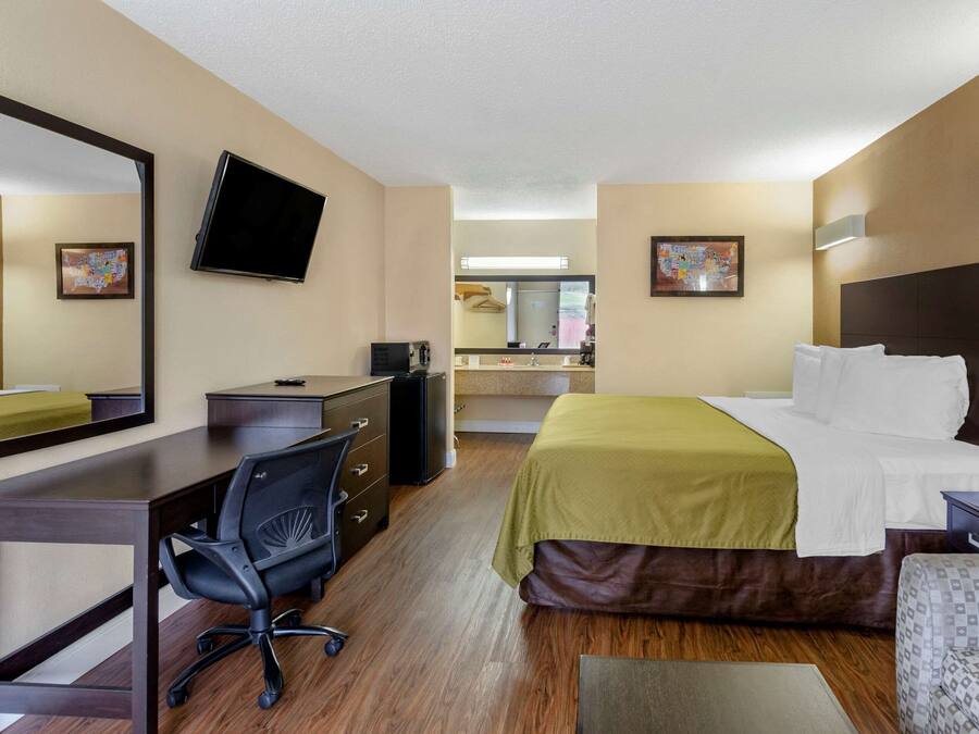 A hotel room with a bed, desk, chair, and a large mirror.