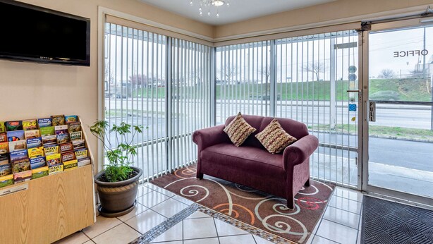 A reception area with a red sofa, a potted plant, a travel information board, and a chandelier. - Econo Lodge Roanoke Civic Center (Roanoke)