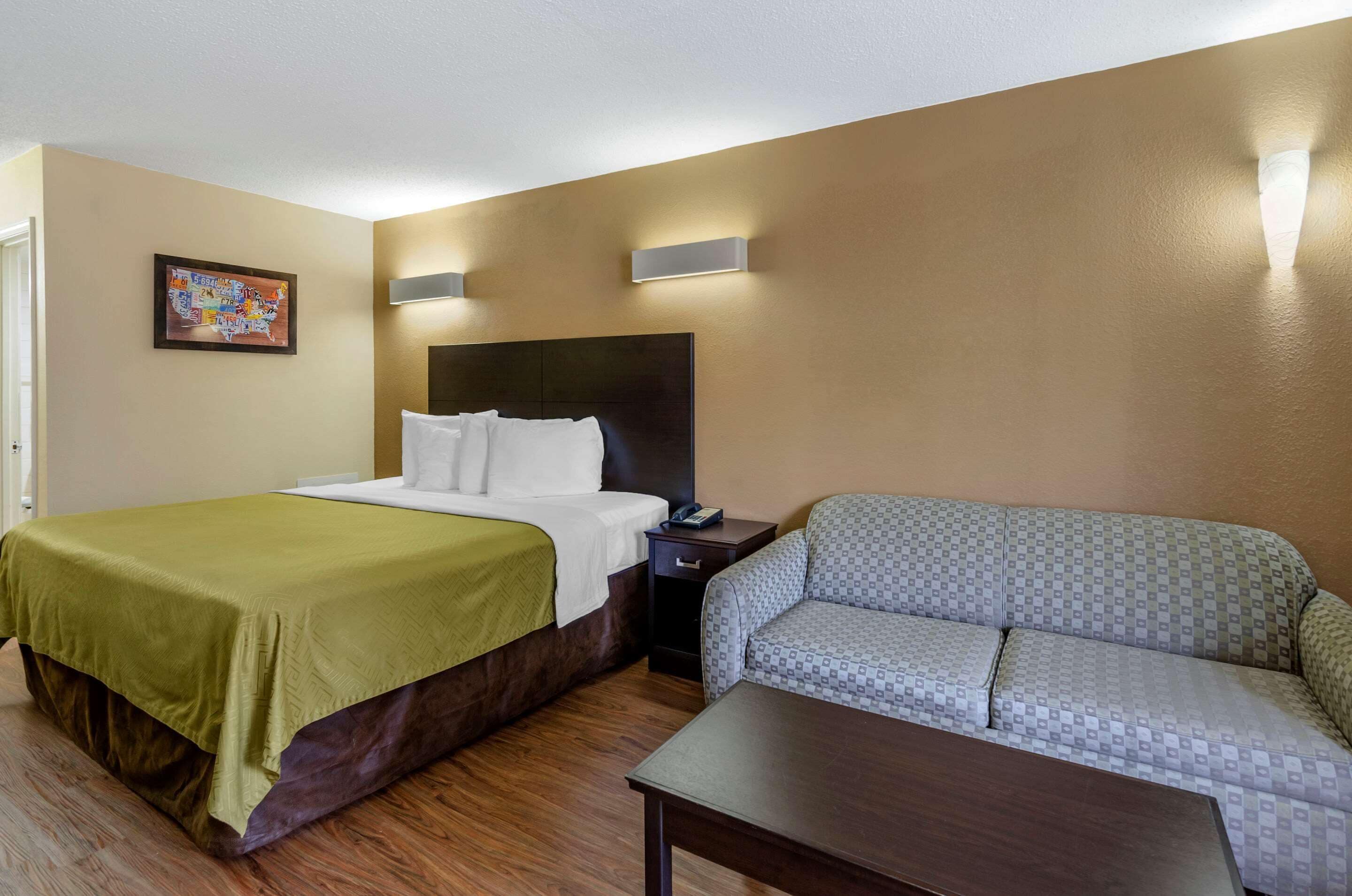 Quarto de hotel com cama, sofá, mesa pequena e mesa de cabeceira.