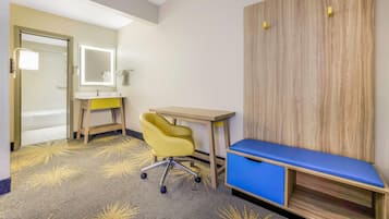A hotel room with a desk, chair, and a bench.