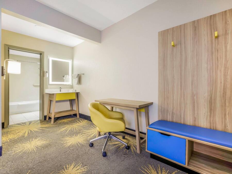 A hotel room with a desk, chair, and a bench.