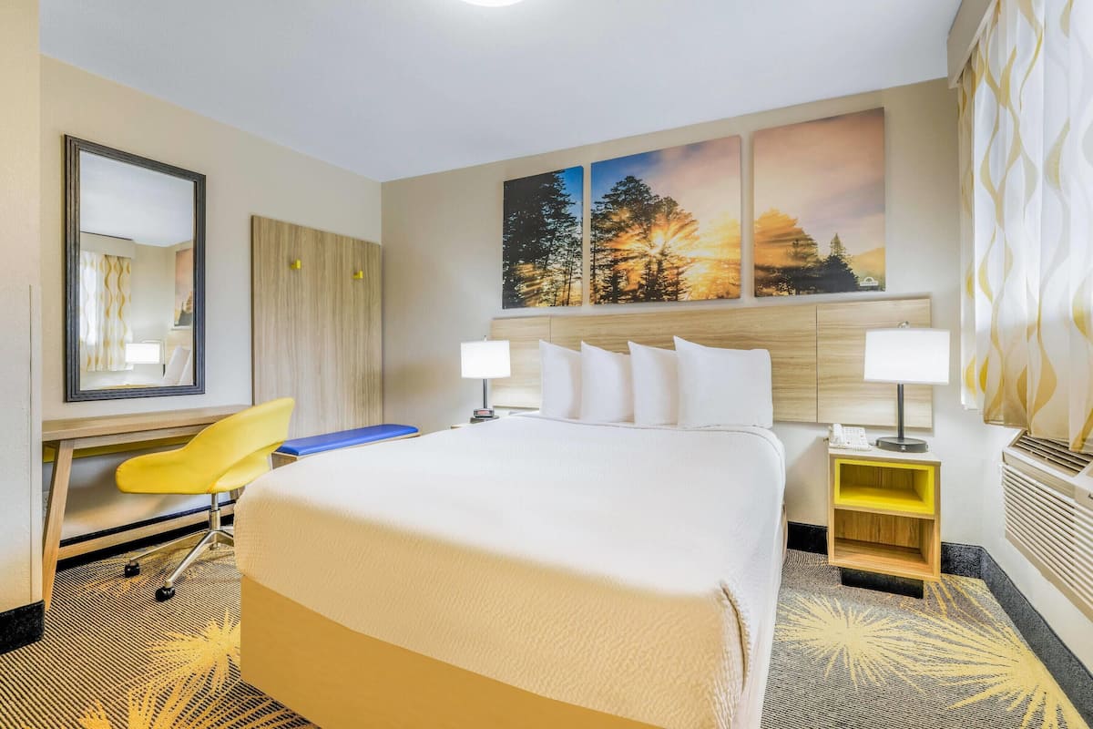 A hotel room with a large bed, a desk with a chair, a nightstand with a lamp, and a wall with three paintings.