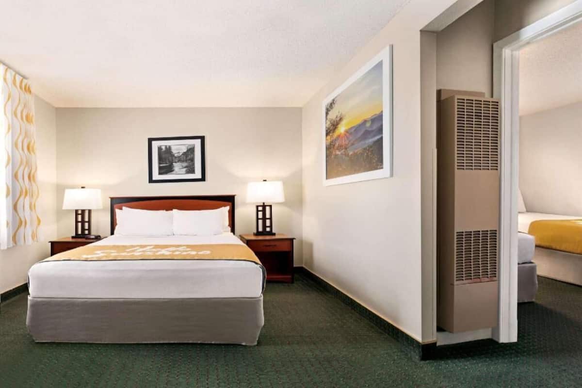A hotel room with a bed, two bedside tables with lamps, a wall-mounted picture, a heater, and a sofa.