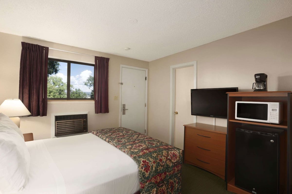 A hotel room with a bed, a desk, a television, a microwave, and a coffee maker.