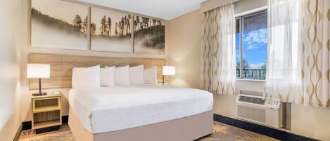 Quarto de hotel com uma cama grande, duas mesas de cabeceira com luminárias, ar condicionado fixado na parede e uma janela com cortinas.