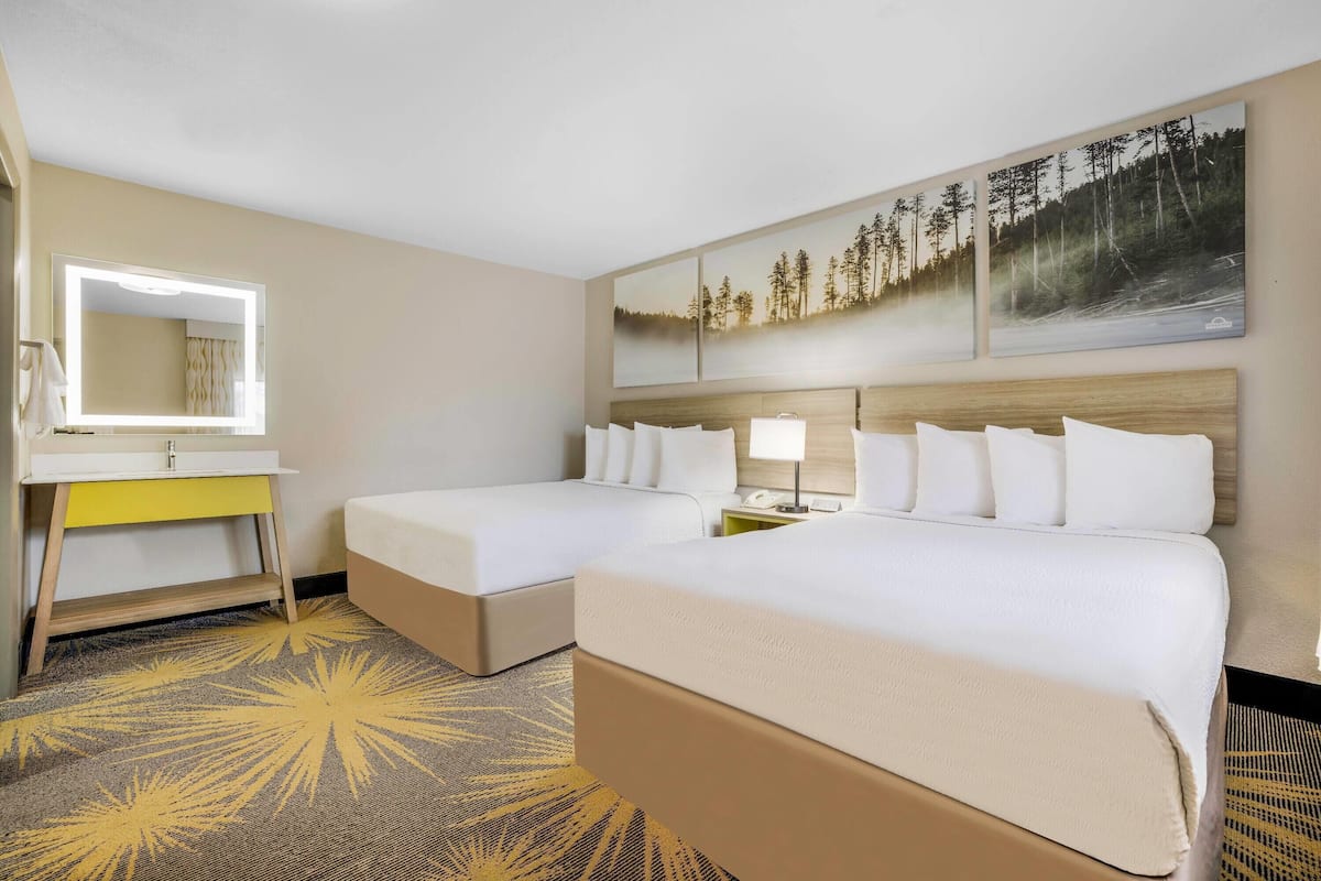 A hotel room with two beds, a bedside table with a lamp, a mirror, and artwork on the wall.