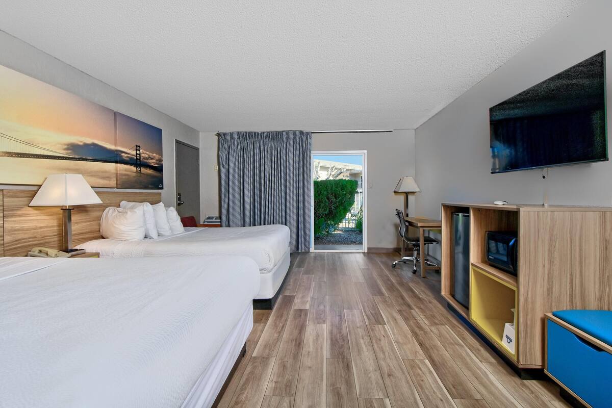 A hotel room with two beds, a desk, a TV, and a large window with a view of a bridge.