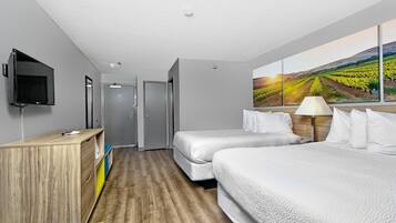 Une chambre d’hôtel avec deux lits, une télévision, un bureau, un miroir et un tableau représentant un vignoble.