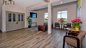 A spacious living area with a wooden floor, a seating area with chairs and a sofa, a dining table with a vase of flowers, and a large window with a view. - Days Inn by Wyndham Novato/San Francisco (Novato)