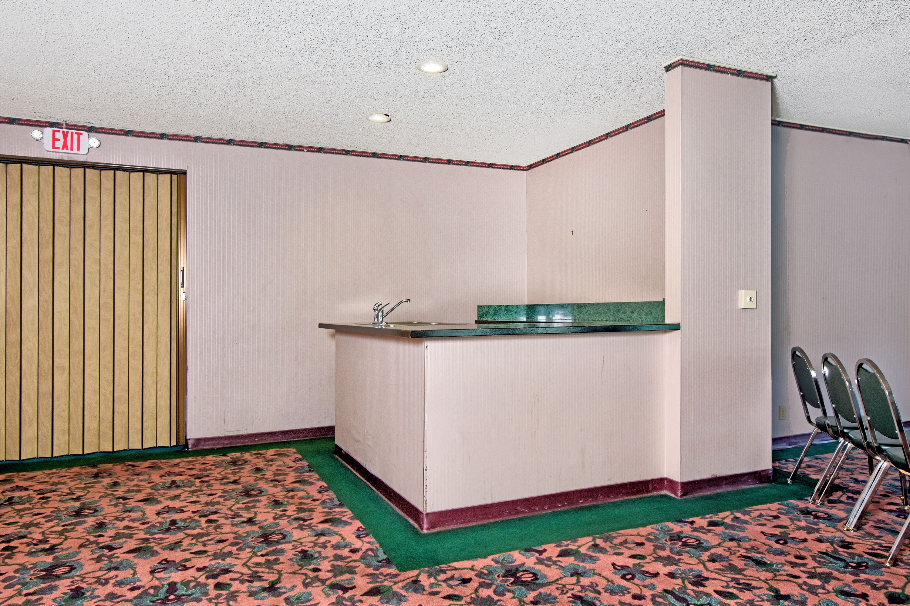 A room with a reception desk, an exit sign, a green carpet, and a wooden door.
