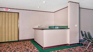 A room with a reception desk, an exit sign, a green carpet, and a wooden door.
