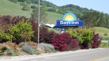 A Days Inn sign with a sun logo, surrounded by landscaped gardens and a hilly backdrop.