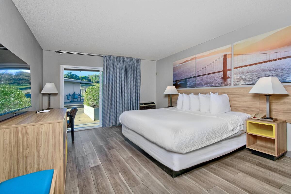 A modern hotel room with a large bed, a desk, and a view of a bridge.