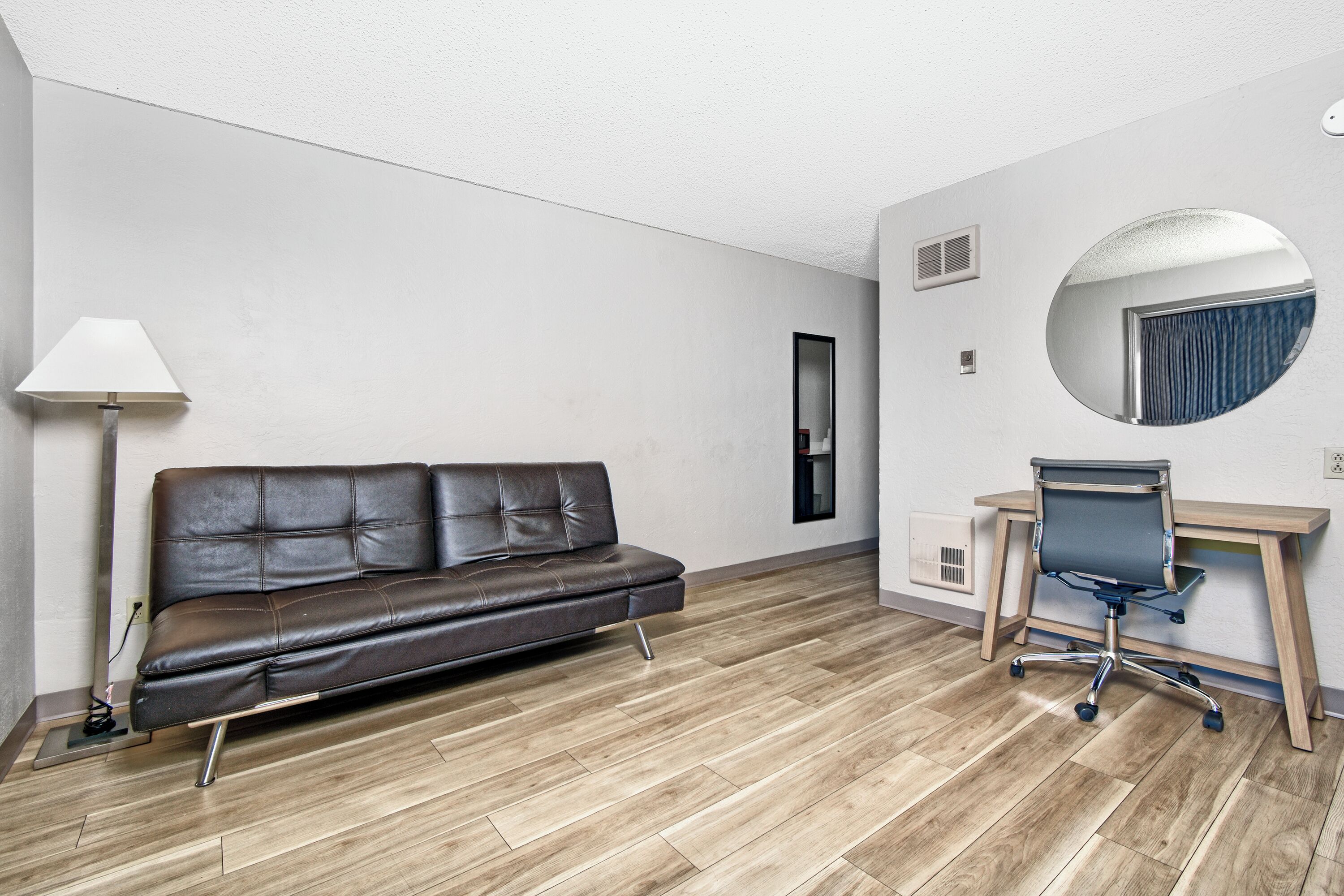 Une pièce moderne avec un canapé en cuir, un bureau avec une chaise, une lampe et un grand miroir rond accroché au mur.