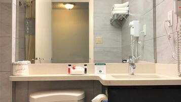 Ein Badezimmer mit Toilette, Waschbecken und Spiegel. Ein Handtuchhalter mit Handtüchern, ein Handtrockner und ein Schild zur Förderung des Umweltschutzes sind vorhanden.