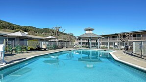 A swimming pool with lounge chairs and umbrellas, surrounded by buildings with a view of hills. - Days Inn by Wyndham Novato/San Francisco (Novato)