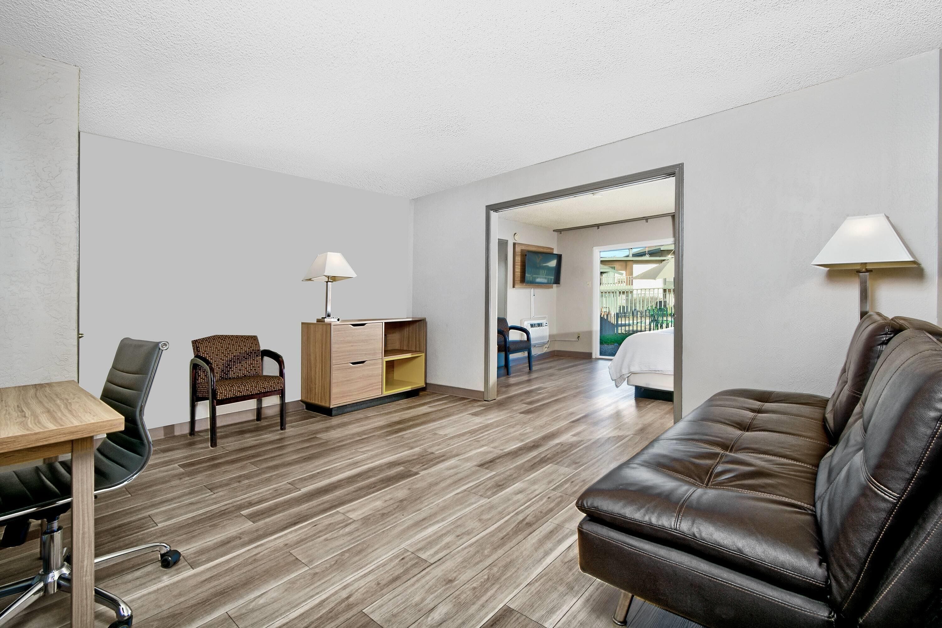 Una sala de estar moderna con un sofá de cuero marrón, un escritorio de madera con una silla, un mueble de madera y una lámpara.