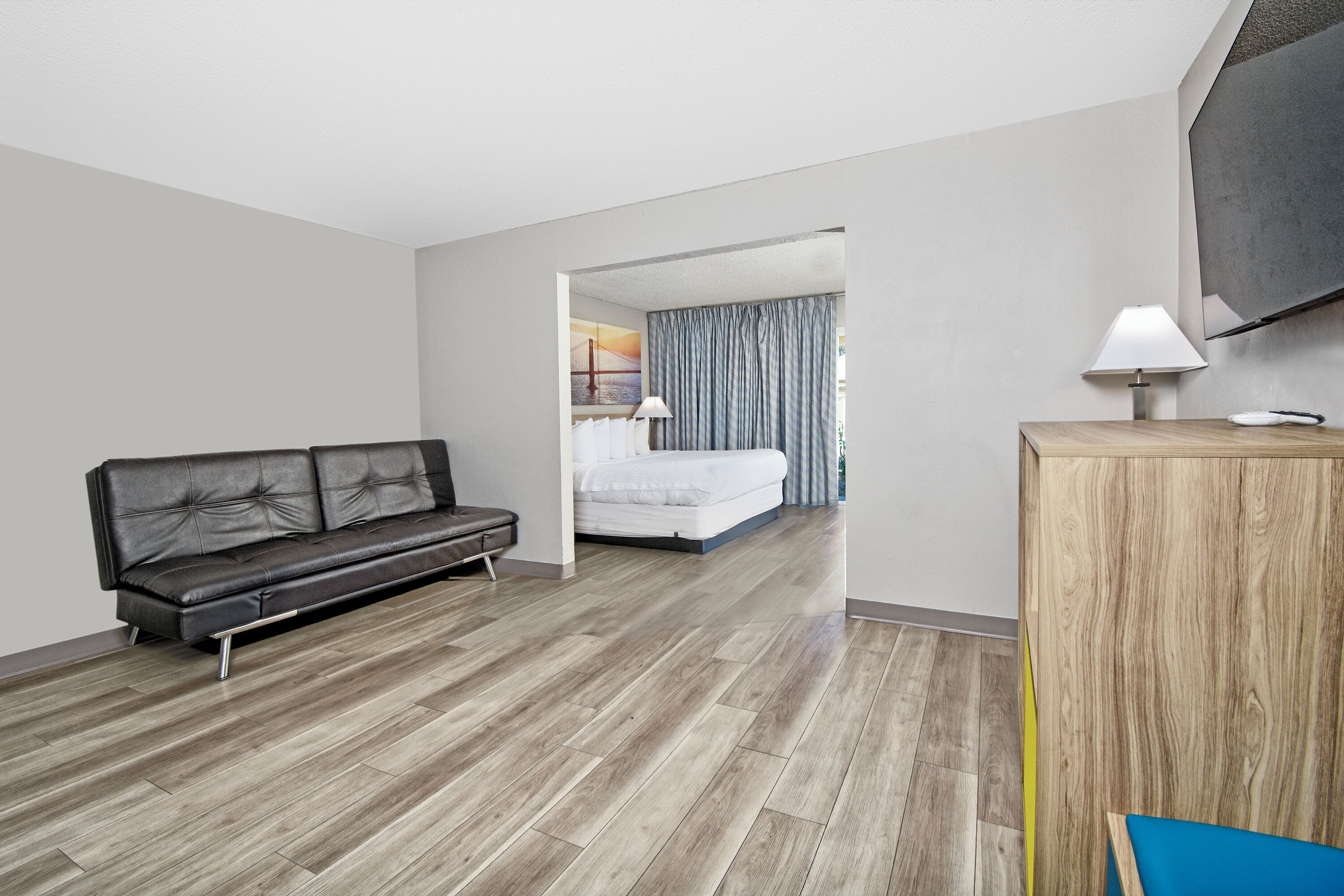 Ein modernes Hotelzimmer mit Ledersofa, Schreibtisch aus Holz, Bett mit Blick und großem Fernseher.