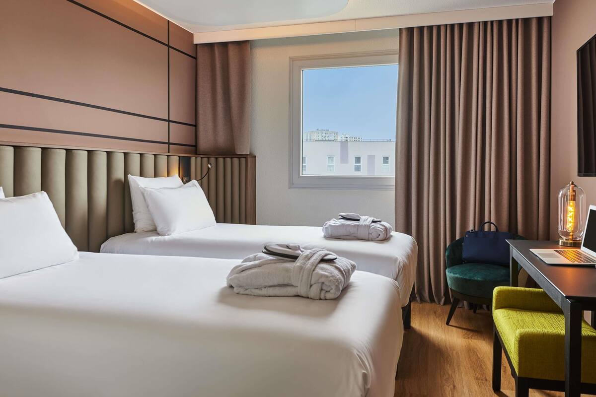 A hotel room with two beds, a desk with a laptop, a chair, and a lamp.