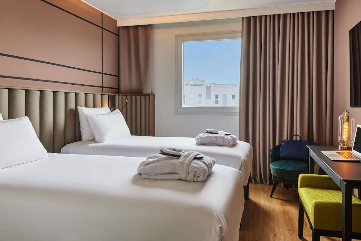 A hotel room with two beds, a desk with a laptop, a chair, and a lamp.