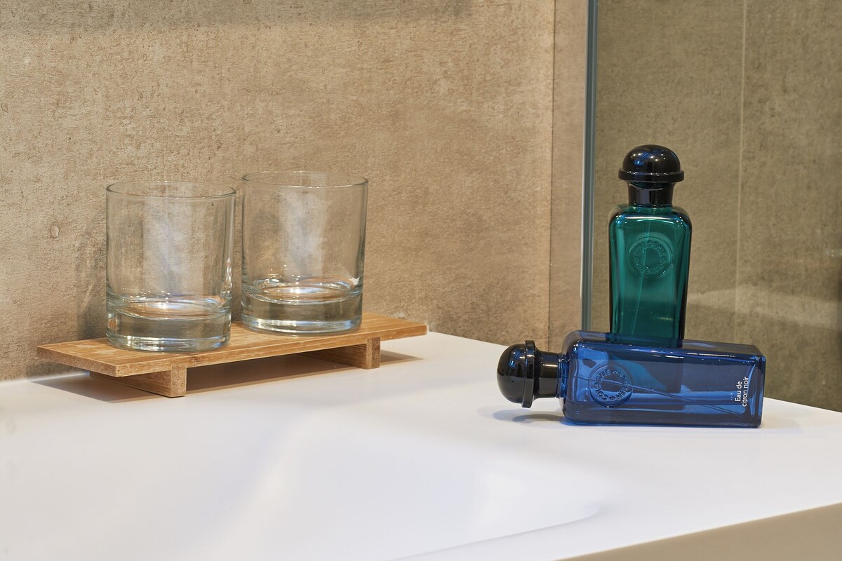A bathroom with a white countertop, two clear glasses, a blue bottle, and a white towel.