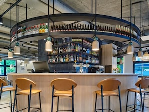 Zona de bar con una estantería curva que exhibe varias botellas, una barra y tres taburetes.