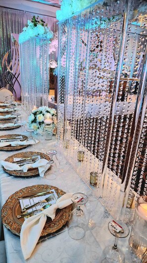 A long banquet table set with ornate gold plates, white napkins, and crystal glasses, surrounded by hanging crystal decorations. - Clarion Hotel BWI Airport Arundel Mills (Hanover)