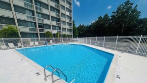 Piscina retangular com grade branca e corrimãos de metal, cercada por um deck revestido com azulejos.