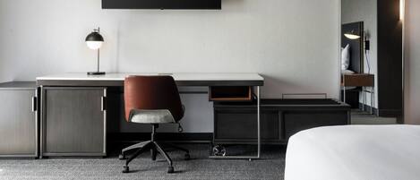 Una habitación de hotel con cama, escritorio, silla, televisión y espejo.