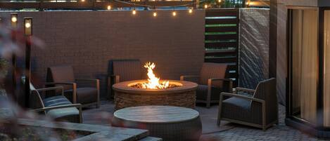 An outdoor patio with a fire pit, wicker chairs, and string lights.