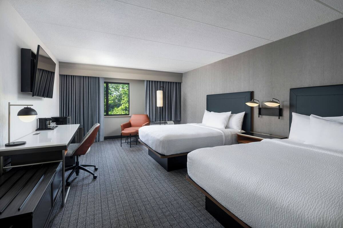 A hotel room with two beds, a desk, a chair, a TV, and a window with curtains.