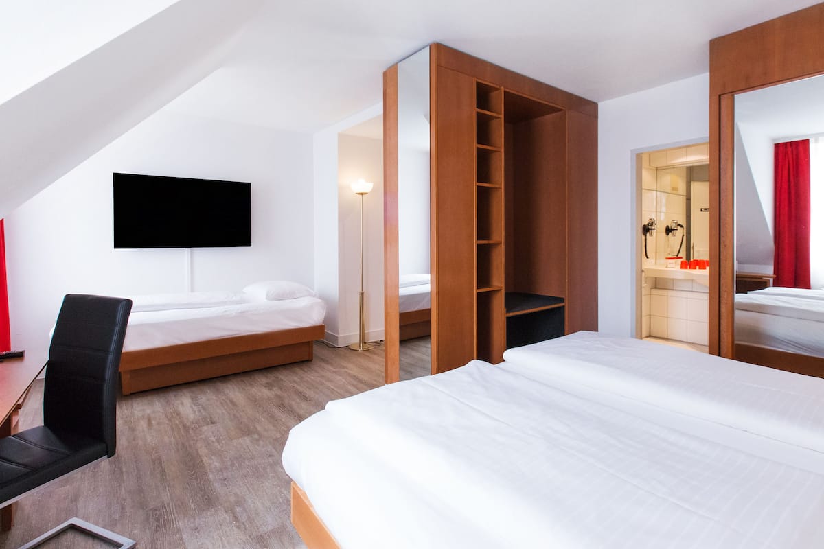 A modern hotel room with a large bed, a desk, a chair, and a TV mounted on the wall.