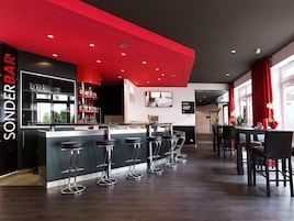 A bar area with a red accent wall, multiple stools, and a bar counter.