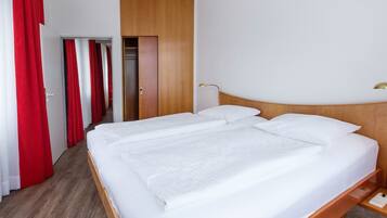 Ein Hotelzimmer mit einem hölzernen Bett, weißer Bettwäsche und roten Vorhängen.