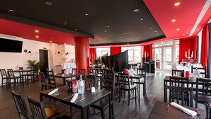 Un restaurante con varias mesas y sillas, un piano y cortinas rojas.