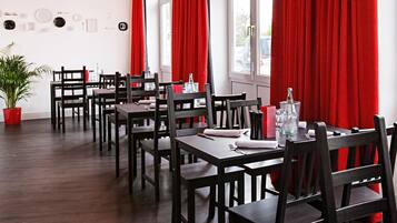 Un restaurante con mesas y sillas de madera, cortinas rojas y una planta en maceta.