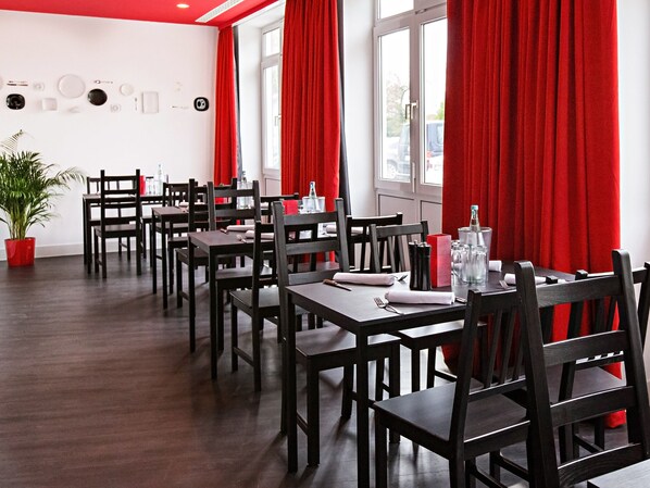 A restaurant with wooden tables and chairs, red curtains, and a potted plant.