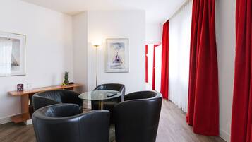 Un salón moderno con una mesa de centro de cristal, sillas de cuero negro, una mesita auxiliar con fruta y cortinas rojas.