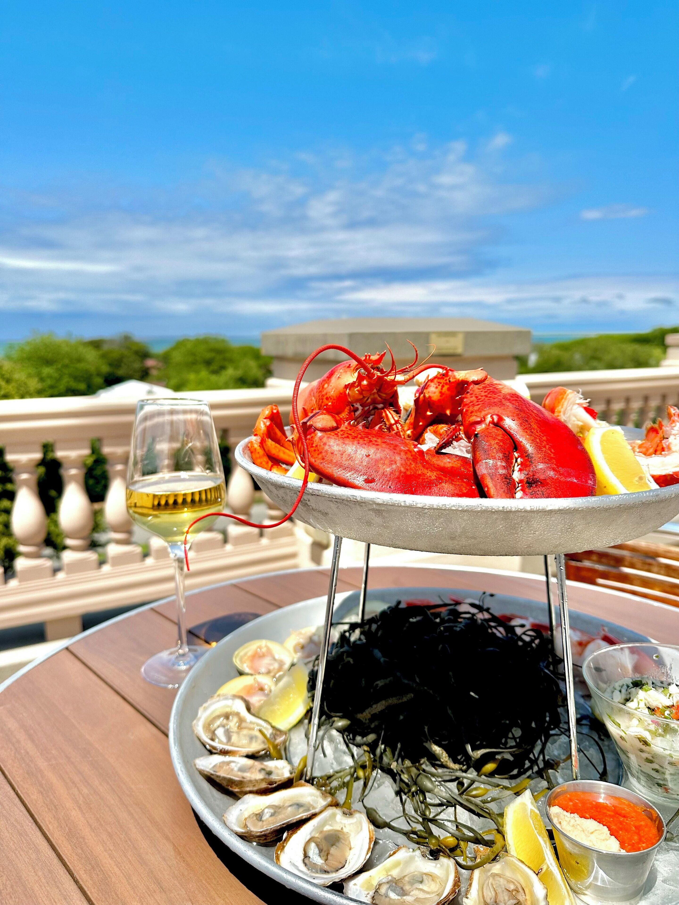 A seafood platter with lobster, oysters, and lemon slices on a table with a glass of white wine.