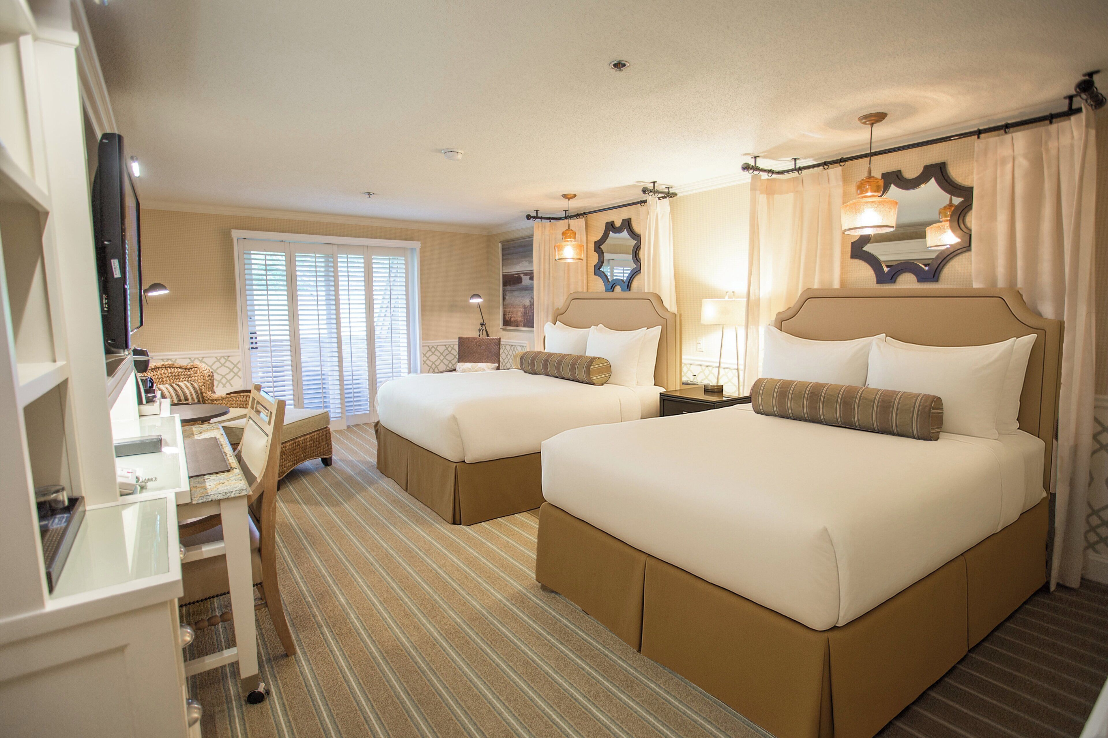 Une chambre d’hôtel avec deux lits, un bureau, une télévision et une fenêtre avec des stores.