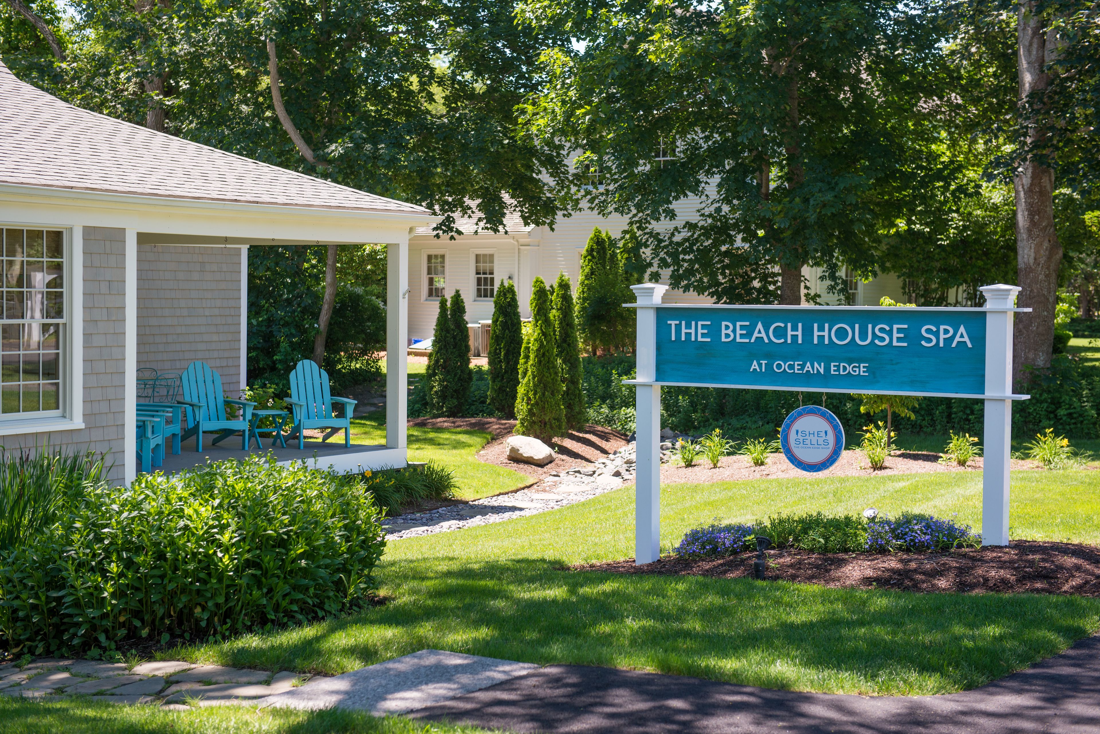 A spa named 'The Beach House Spa' with a sign, outdoor seating, and a well-maintained garden.