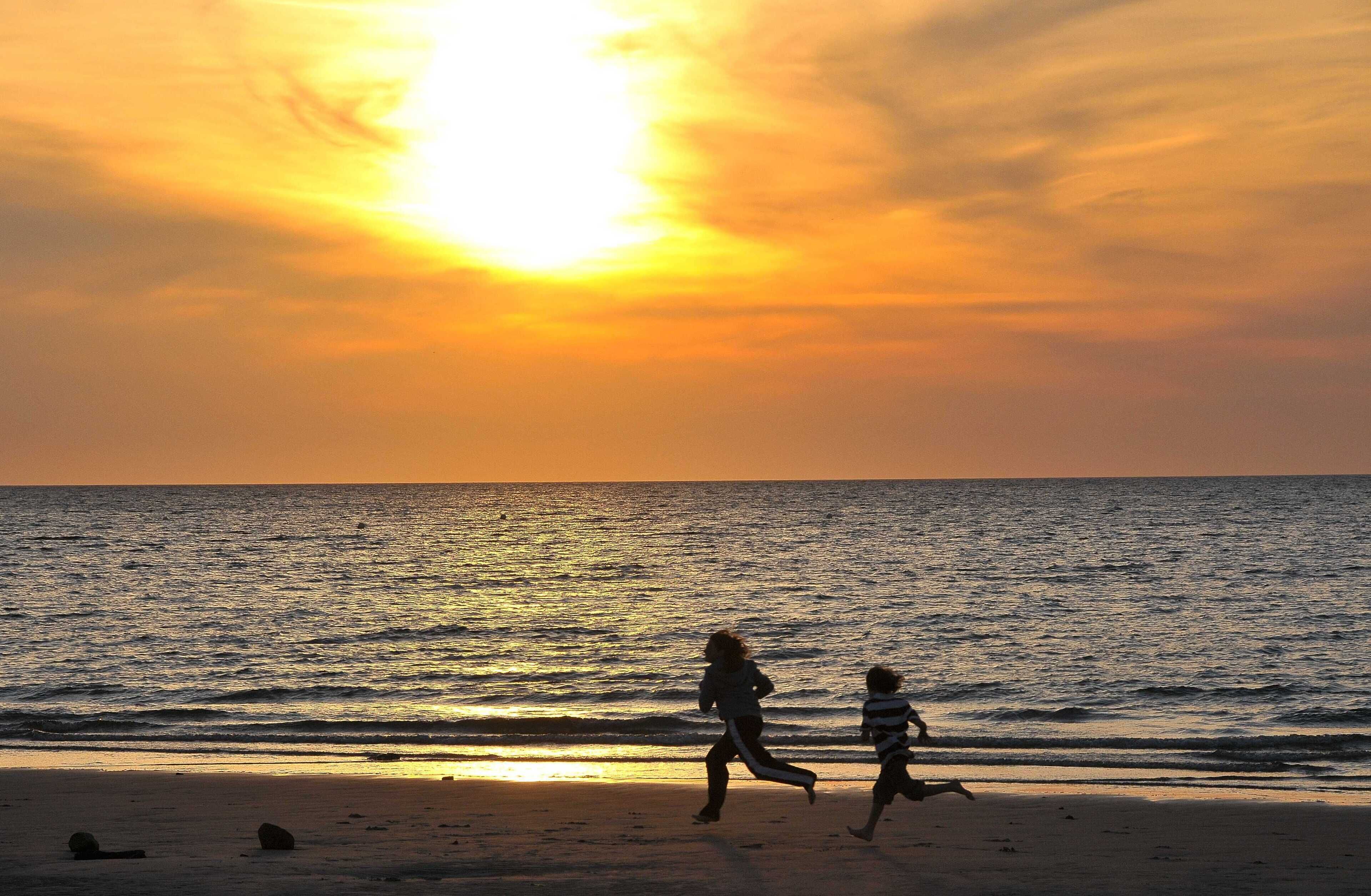 A sunset over the ocean with silhouettes of people running on the beach.